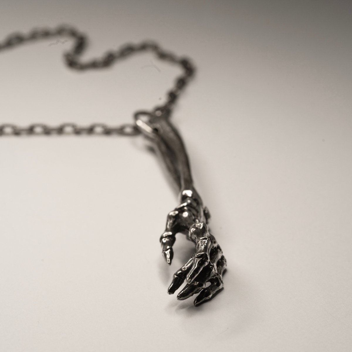 Silver Skeleton Arm pendant lying on a white surface 