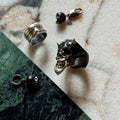 Masked Skull ring — black marble variant — styled with Waves ring and Ancient Skull Charm on a marble surface