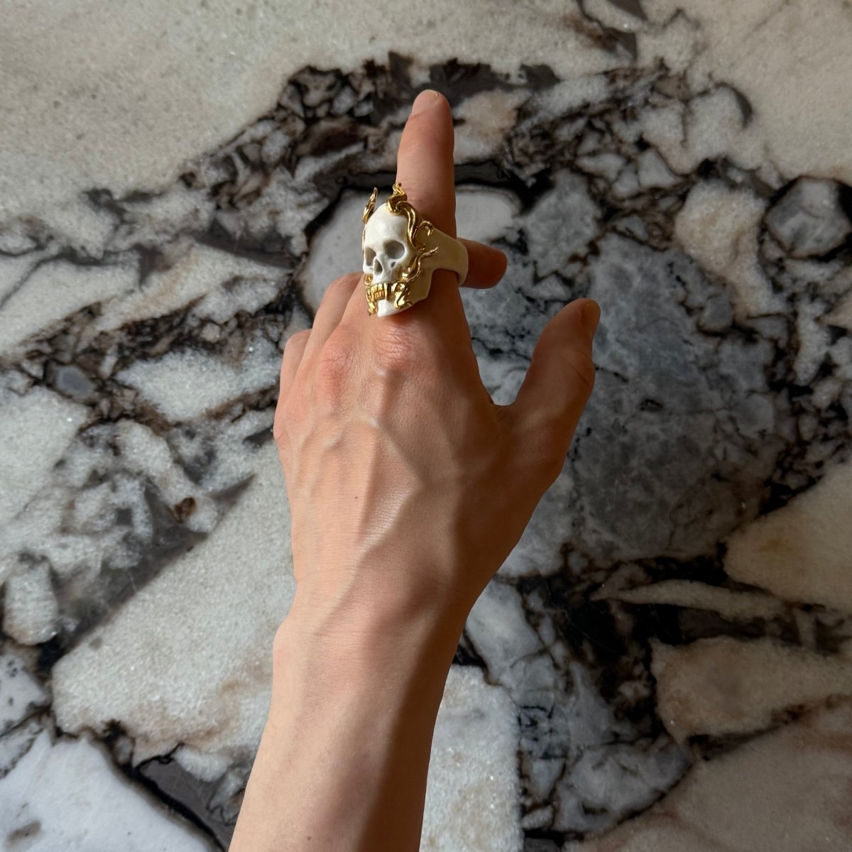 Mayla Skull ring by Macabre Gadgets on a man's hand, in front of stunning white marble background