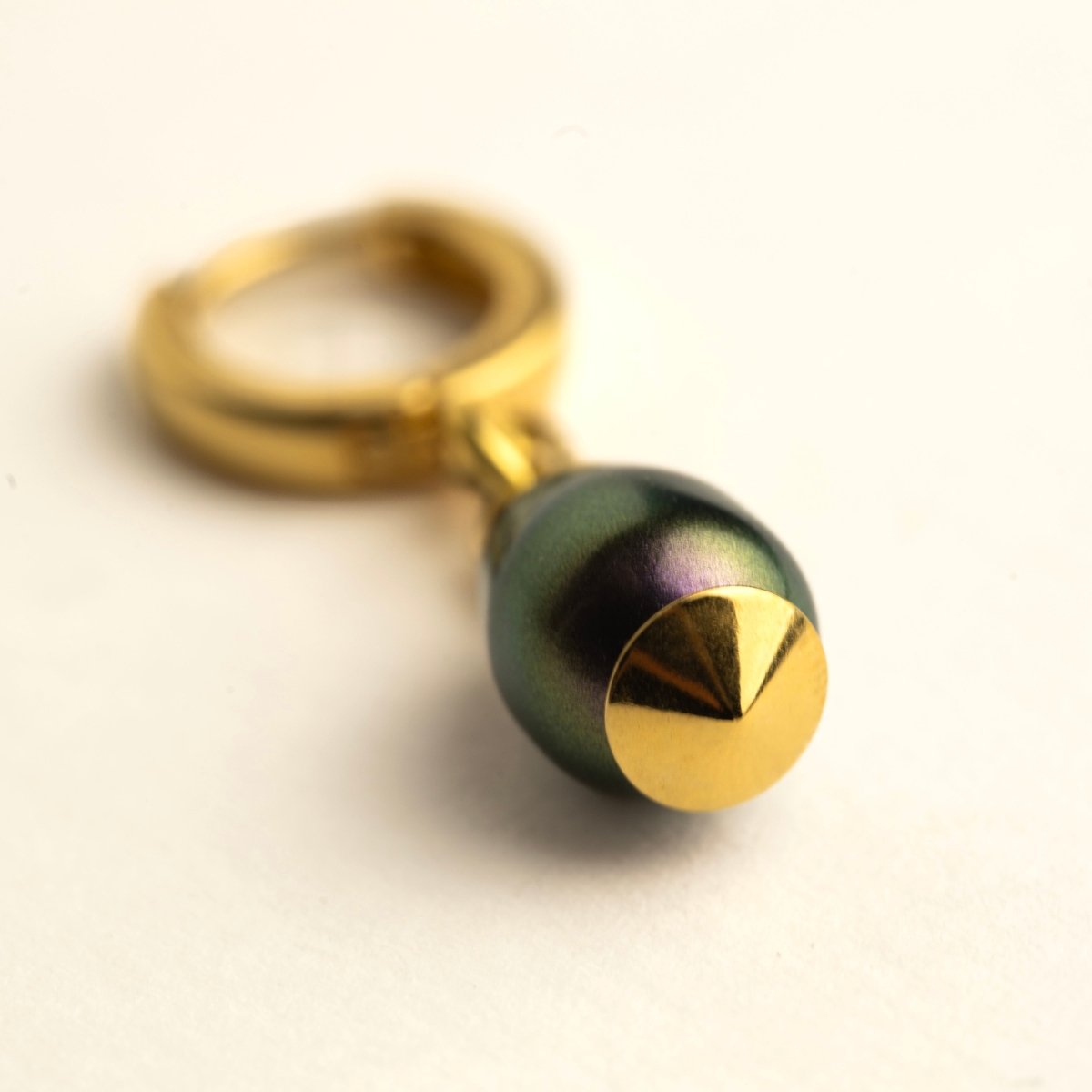 Olive Pearl earring lying on a white surface with focus on the rich dark green colour of the pearl