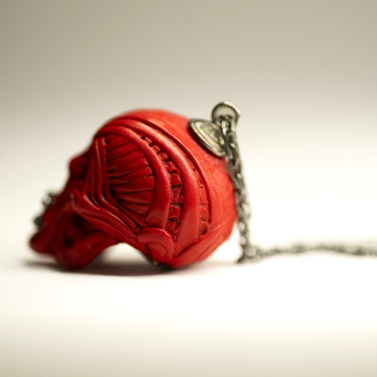 Ornate Skull pendant placed on white surface, showing fixture and chain, as well as marble relief