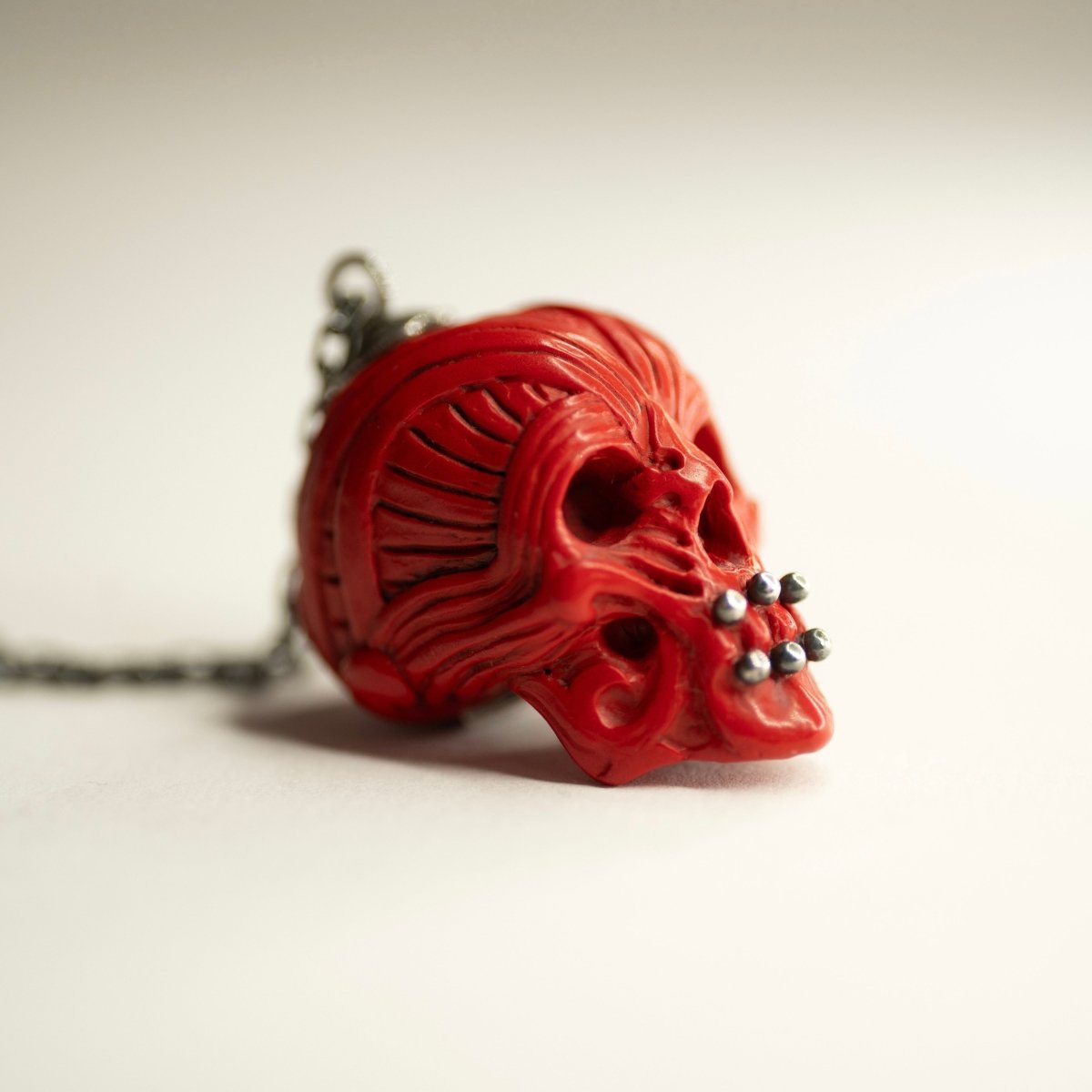 Ornate Skull pendant, semi-profile, pendant placed on a white surface, red variant