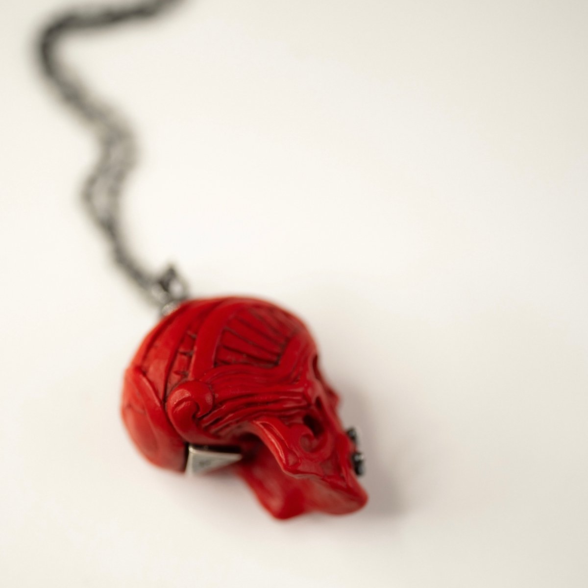Ornate Skull pendant placed on the white surface on its side, to show the relief decoration from different angle