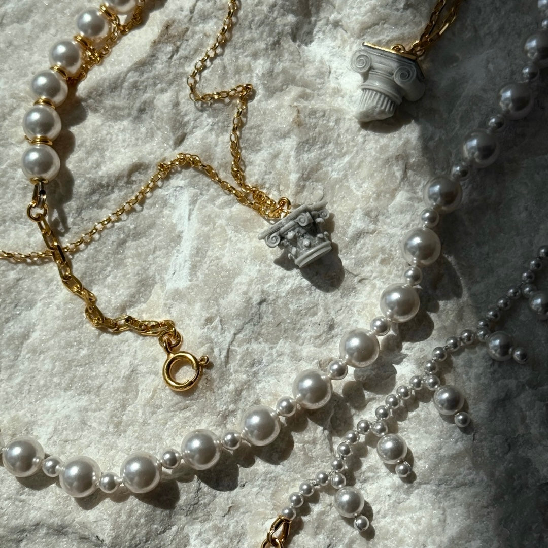 Corinth and Ionic pendants and pearls chokers handcrafted by Macabre Gadgets on a white Carrara marble surface