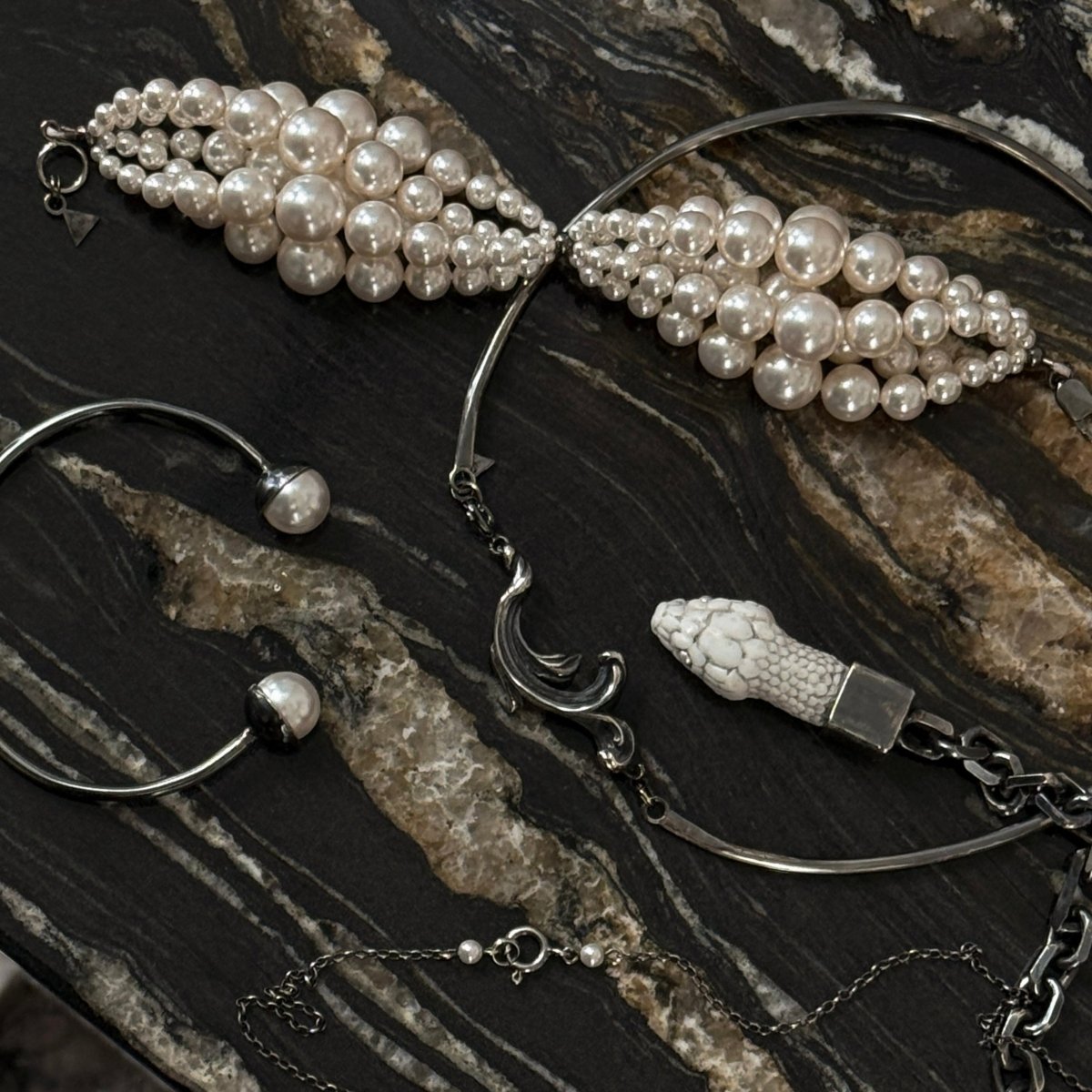 Multi-strand Pearl bracelet with along with the other jewelry by Macabre Gadgets on a dark marble surface