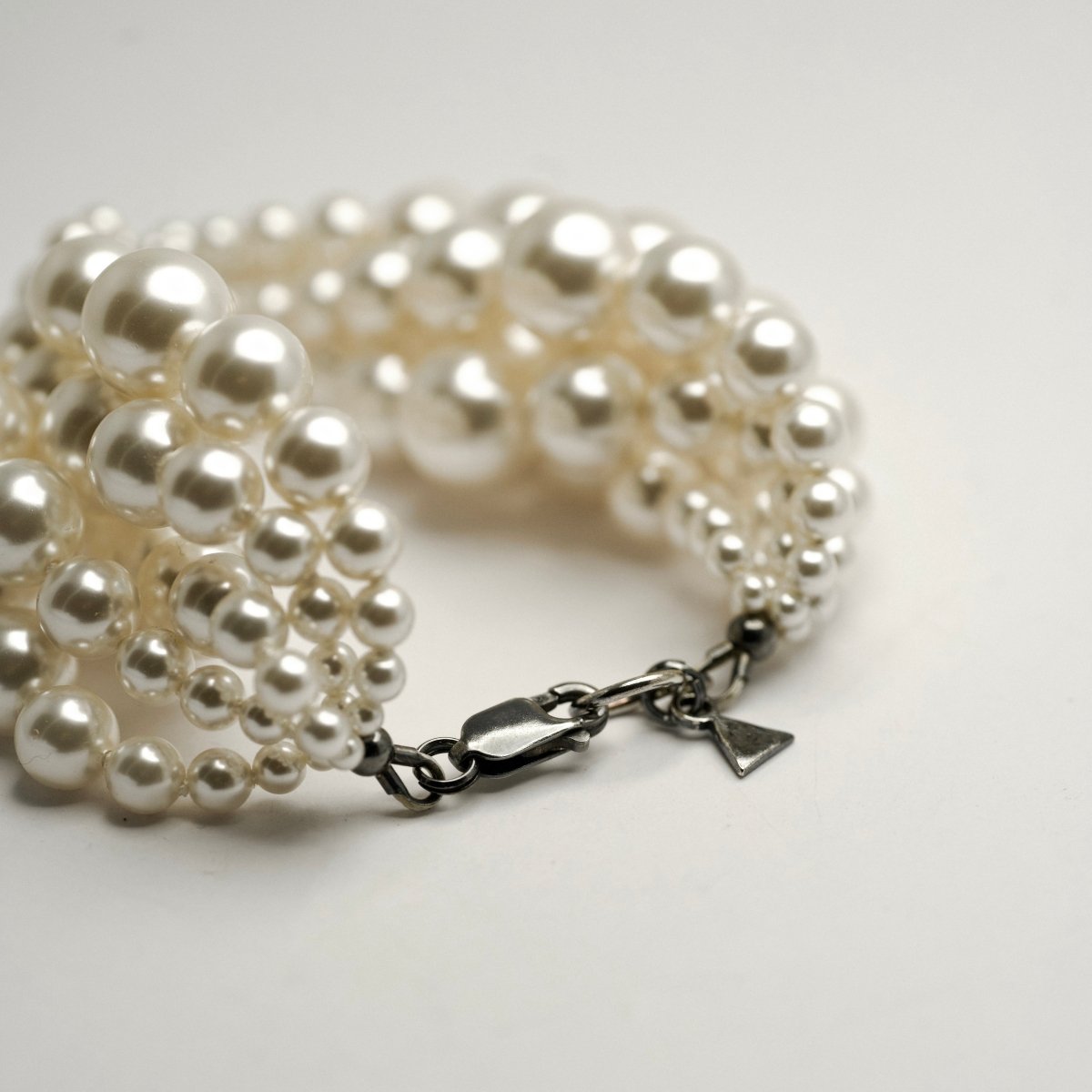 Multi-strand Pearl bracelet placed on a white surface, close up of the lobster clasp and sterling silver logo detail