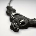 Close-up of Serpent necklace - shaped like black coiled snake with silver stars and moon on its body and placed on white surface