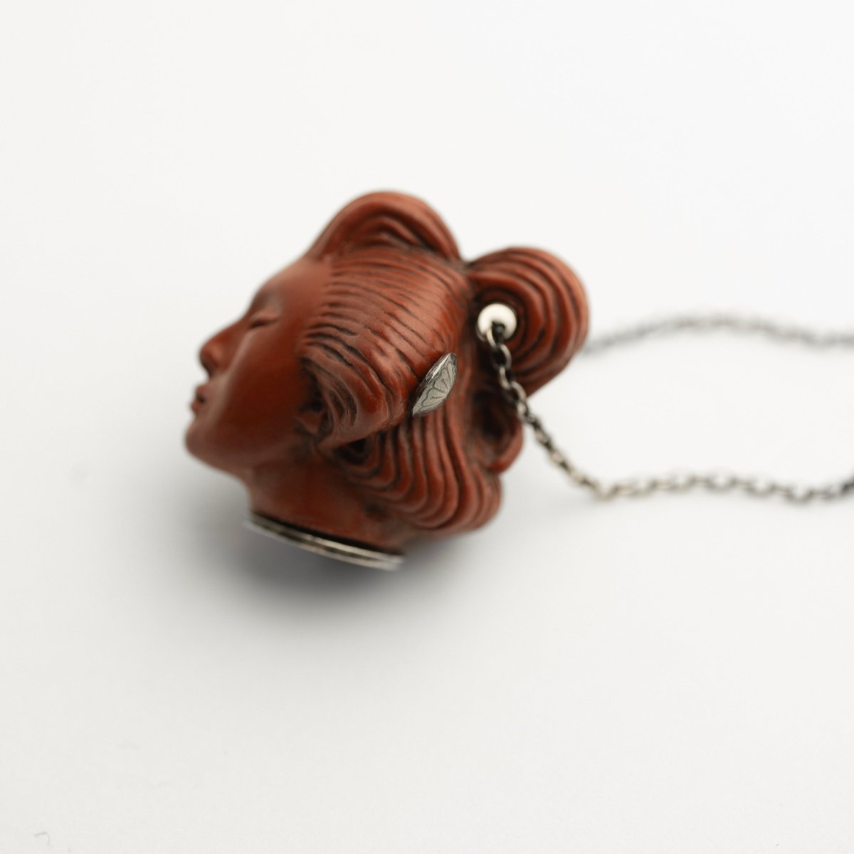 She pendant, terracotta variant, lying on a white surface, sterling silver decorations are visible 