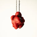 She pendant, red variant, on a chain against white background, shows how the hair knot on the sculpted head becomes a functional feature, holding a chain.