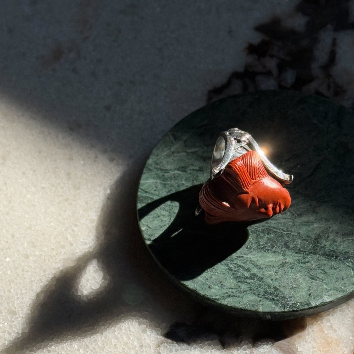 She ring - terracotta variant -placed on a few marble slubs with sunlight reflecting from its polished silver and marble surfaces