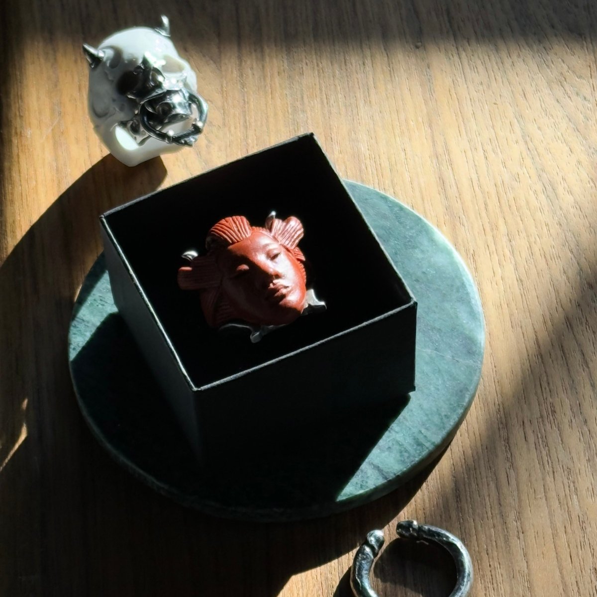 She ring - terracotta variant - in the jewelry box, along with Masked Skull ring and Janus ring by Macabre Gadgets on a wooden surface