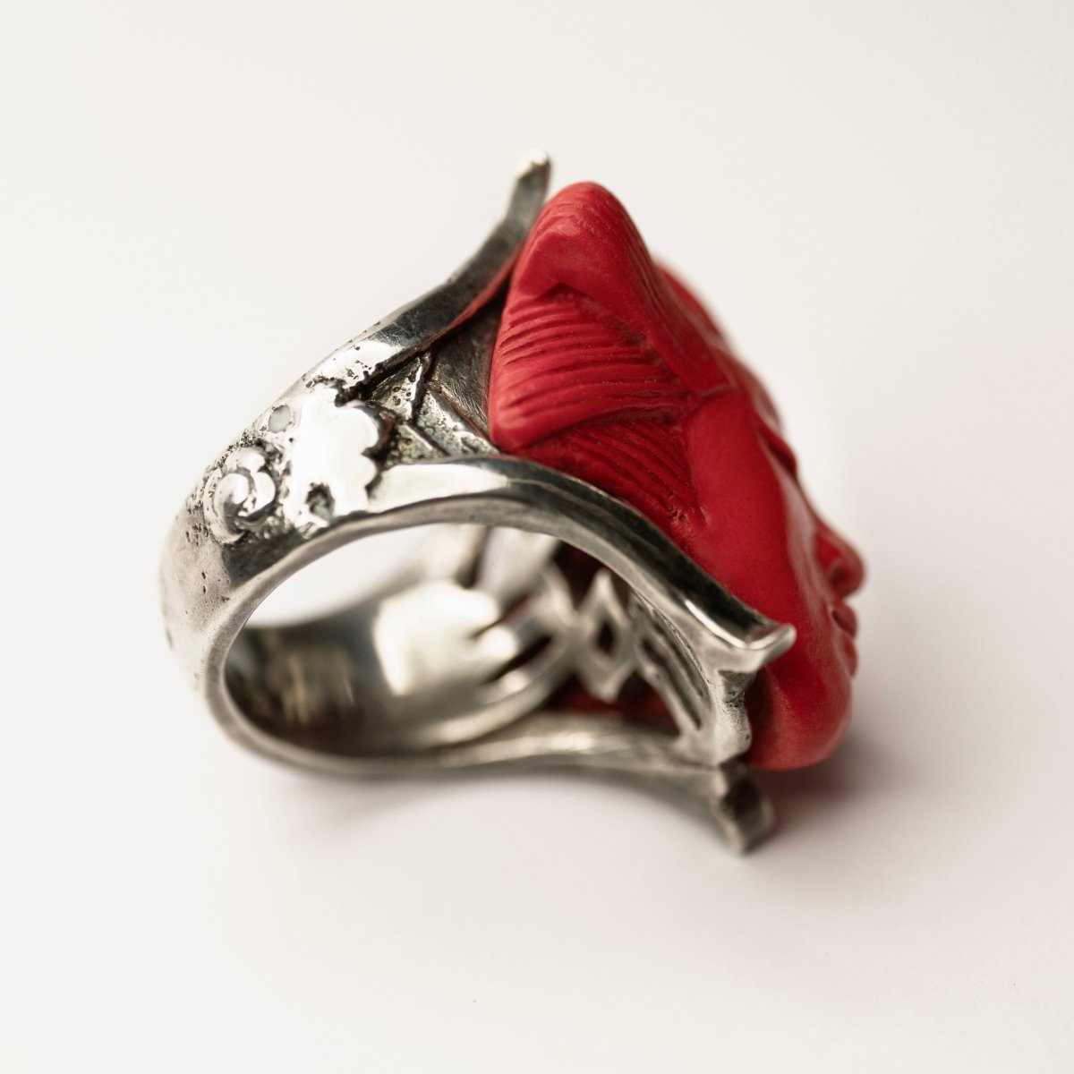 She ring - red variant - on a white surface, focus on the ring rich details, its texture and antique finish