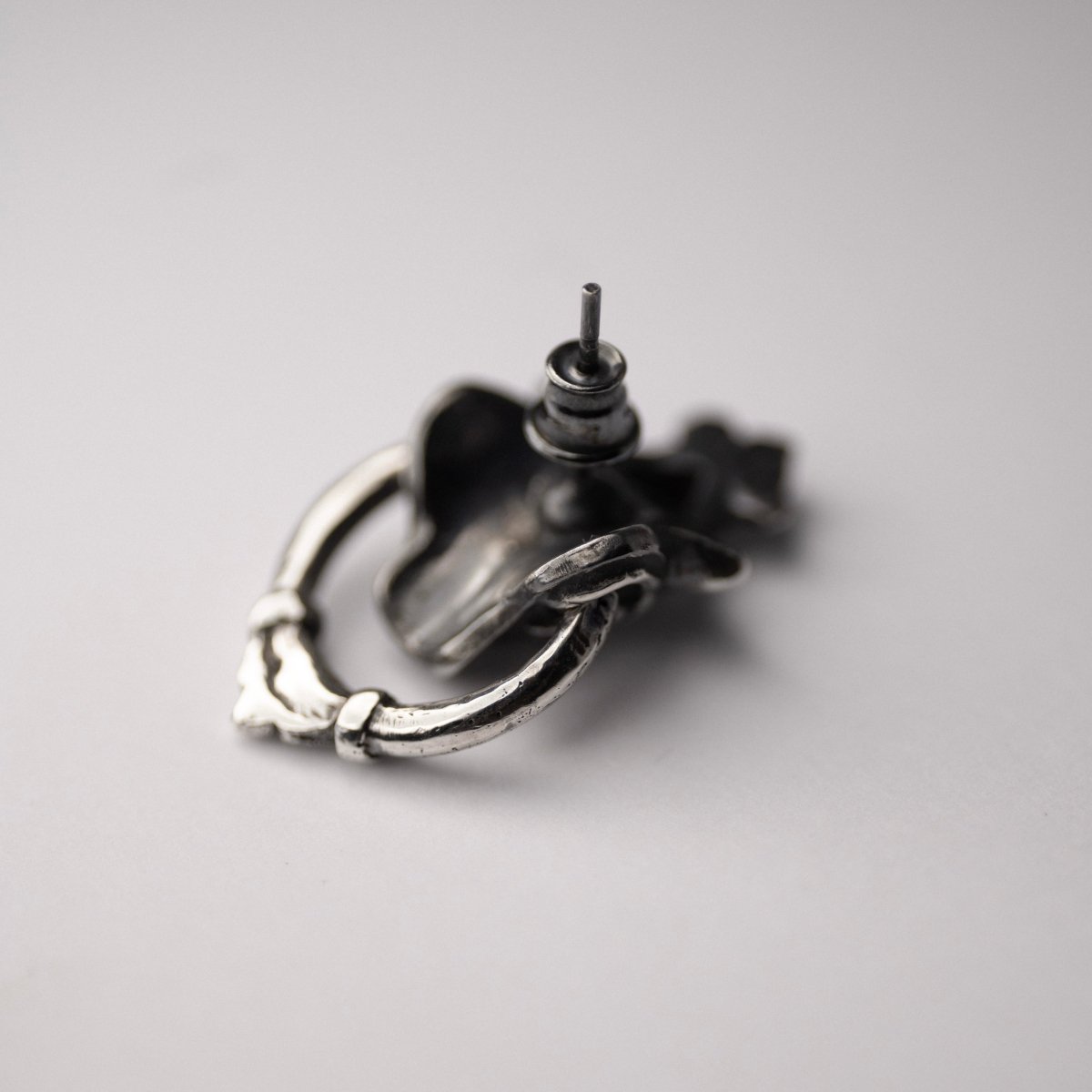 Silver Mask earring — placed upside-down on white surface showing stud lock and back construction