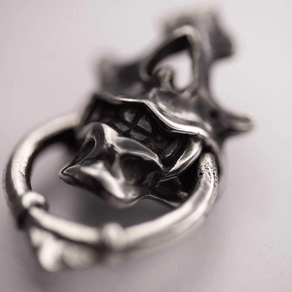 Silver Mask earring — close up on ornamental ring gripped in sharp teeth, netsuke-inspired detailing