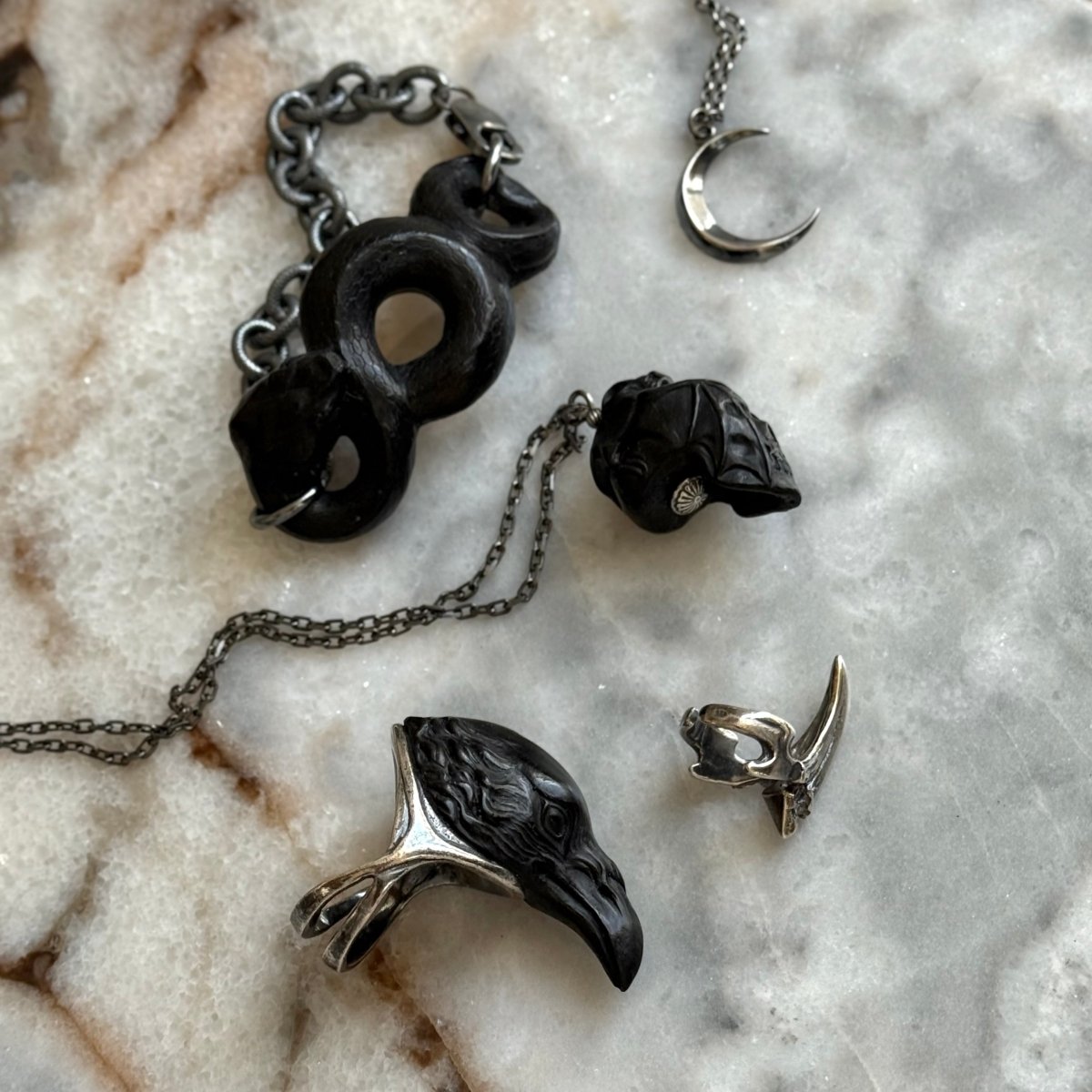 Skull & Bat pendant - black variant - on a light marble surface, along with Snake bracelet and Raven ring by Macabre Gadgets