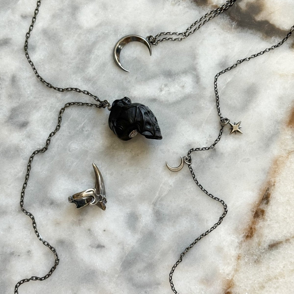 Skull & Bat pendant placed on a marble surface with other jewelry by Macabre Gadgets