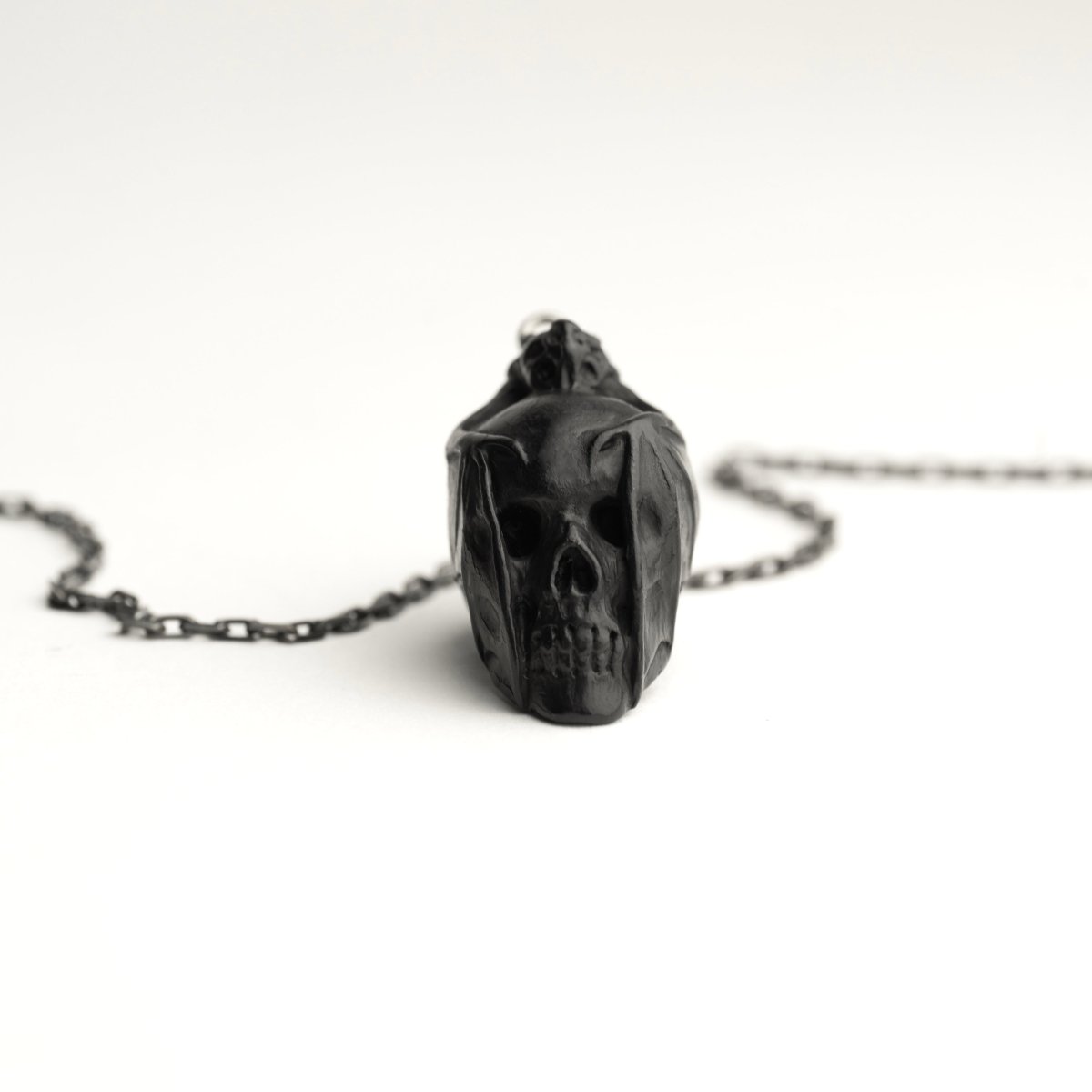 Skull & Bat pendant - black variant - placed on a white surface, skull's sculpted details are clearly visible, front view