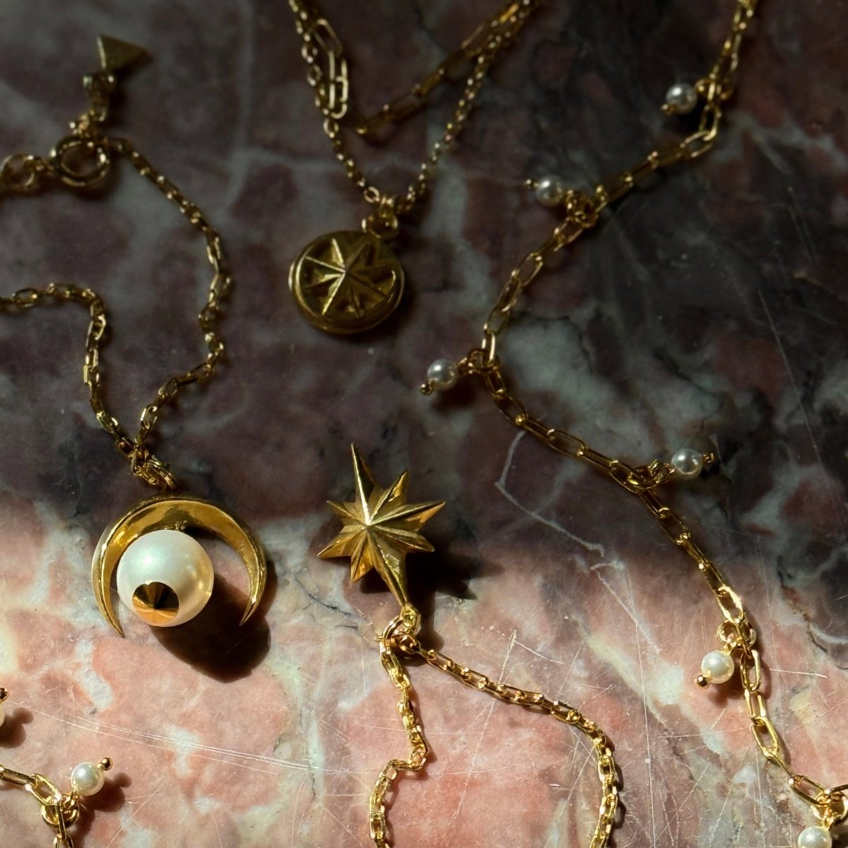 Star bracelet, Moon bracelet, Ancient Pearl bracelet and Aster bracelet placed on a pink marble surface