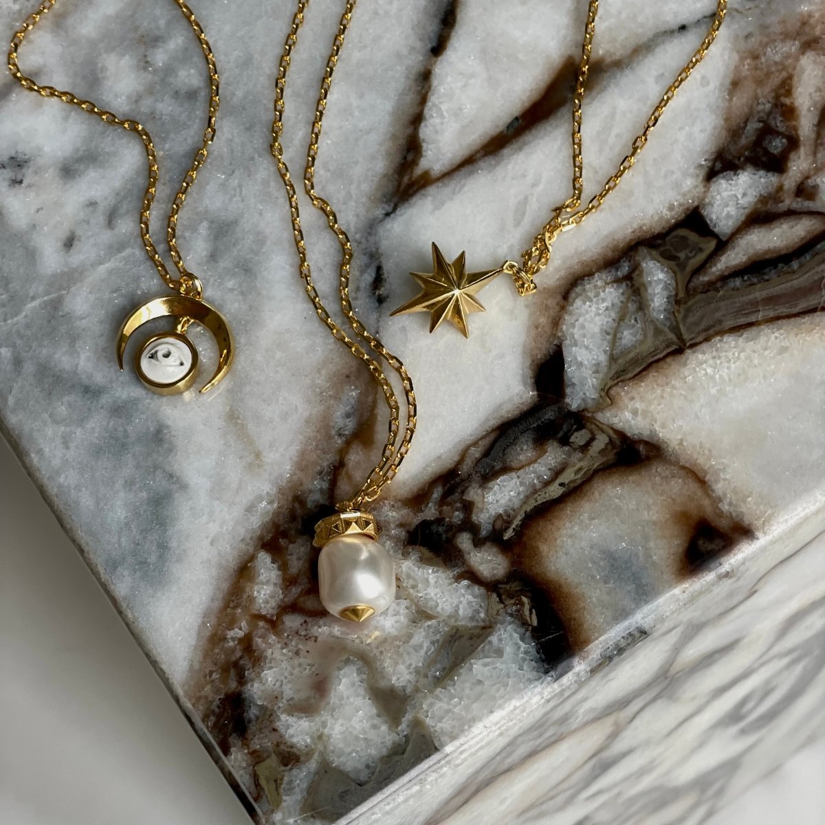 Gold star pendant with Macabre Gadgets pendants on marble block — celestial jewelry styling