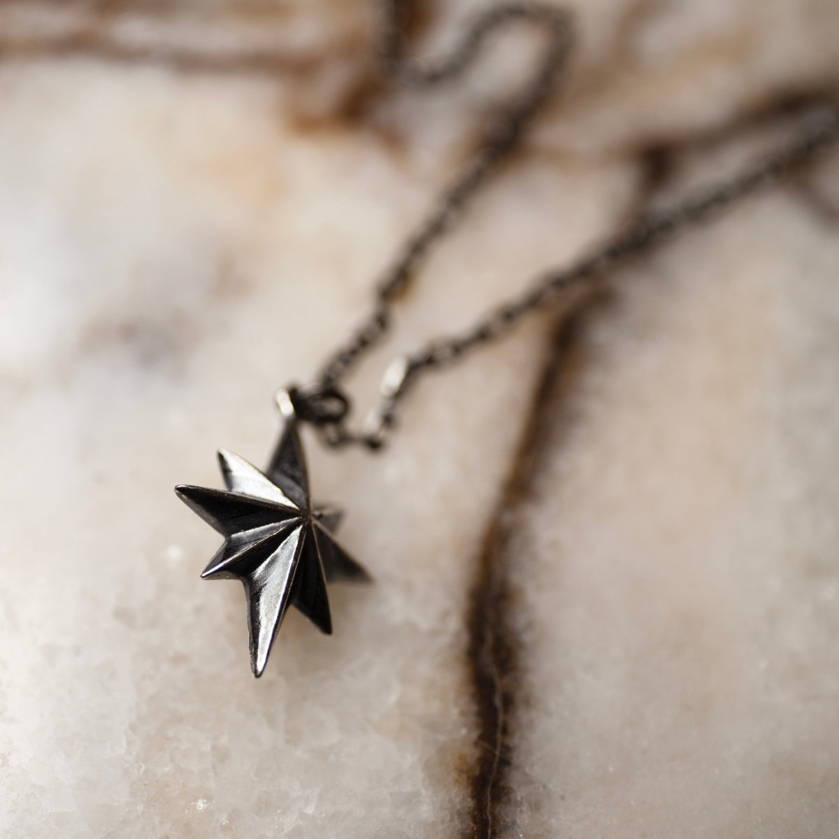 Star pendant silver — close-up of mirror-polished 8-point geometric star on marble surface