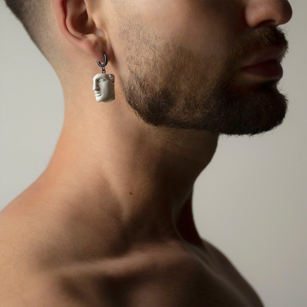 Male model wearing Achilles earring with white marble sculpture fragment by Macabre Gadgets, ancient Greek mythology jewelry lifestyle shot
