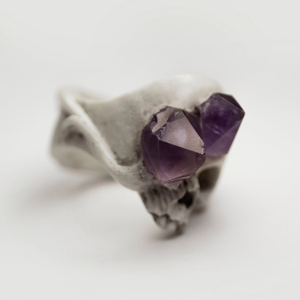 Amethyst Crystal Skull Ring placed on white surface, light reflecting on amethyst crystals 