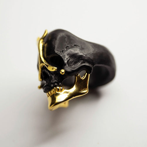 Ancient skull ring - black - gold variant, placed on a white surface, focus on gilded jaw of the skull