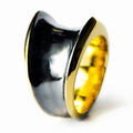 This image features the "Armour I ring," a striking piece of jewelry that combines oxidised sterling silver and 24K gold plating. The ring showcases a unique, handcrafted design with a dramatic contrast of black exterior surfaces and a  yellow gold interior, which enhances its visual appeal