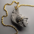 Athena pendant - placed on a white surface, with elaborate decoration of helmet and hair details in focus 