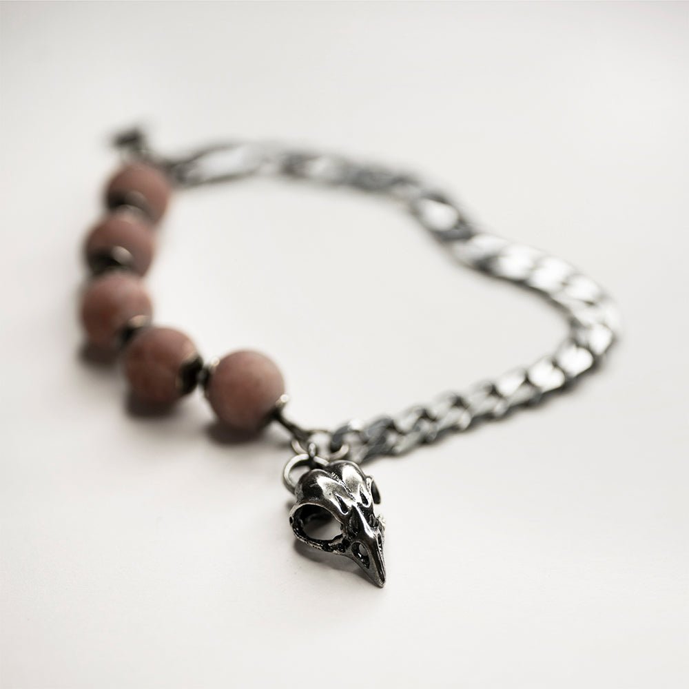 Bird Skull Bracelet on a white surface, bird skull charm and pink quartz beads are visible, the chain is blurry