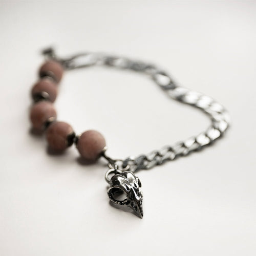 Bird Skull Bracelet on a white surface, bird skull charm and pink quartz beads are visible, the chain is blurry