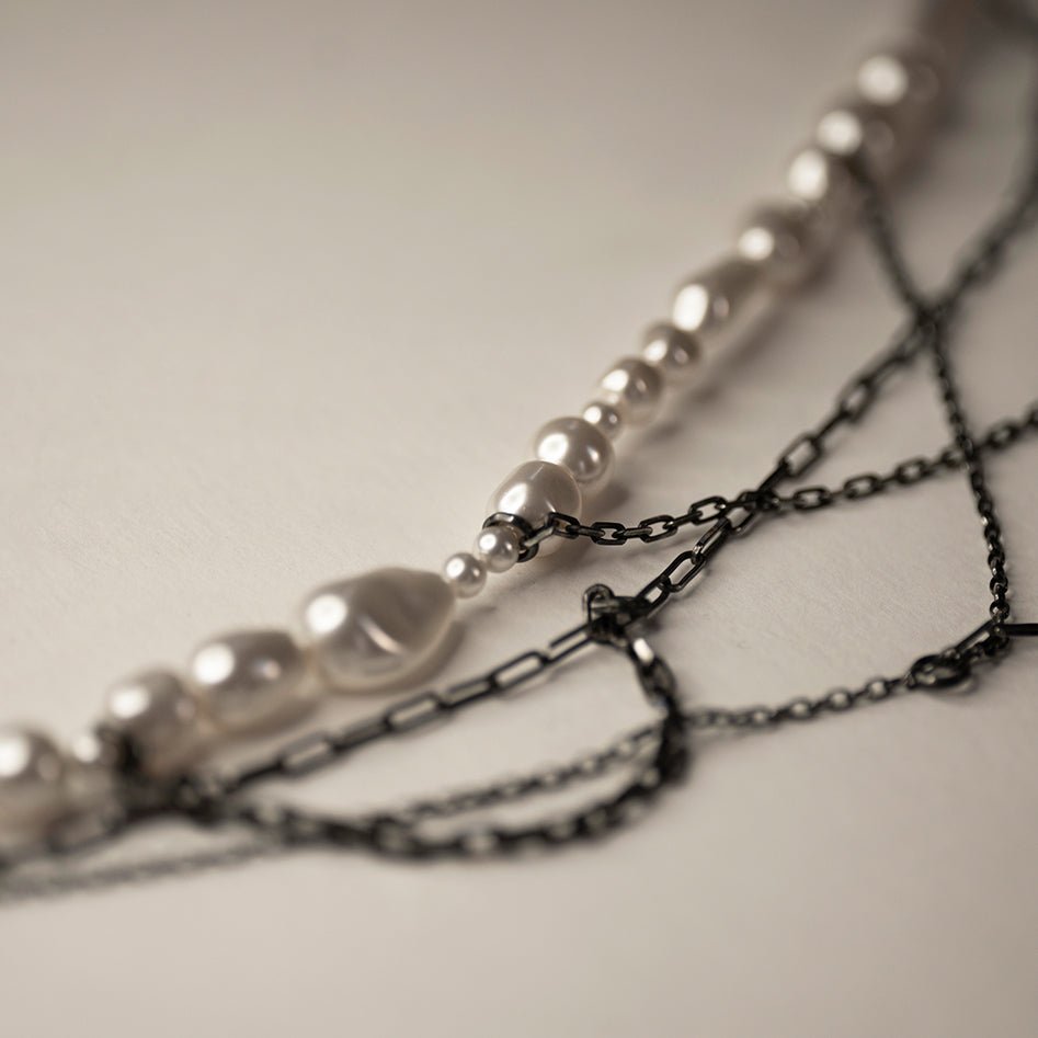 Dew necklace placed on beige surface, close-up of different pearls and chains