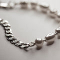 Double bracelet - close up - focus on a flat curb chain and its fixture to the pearl part