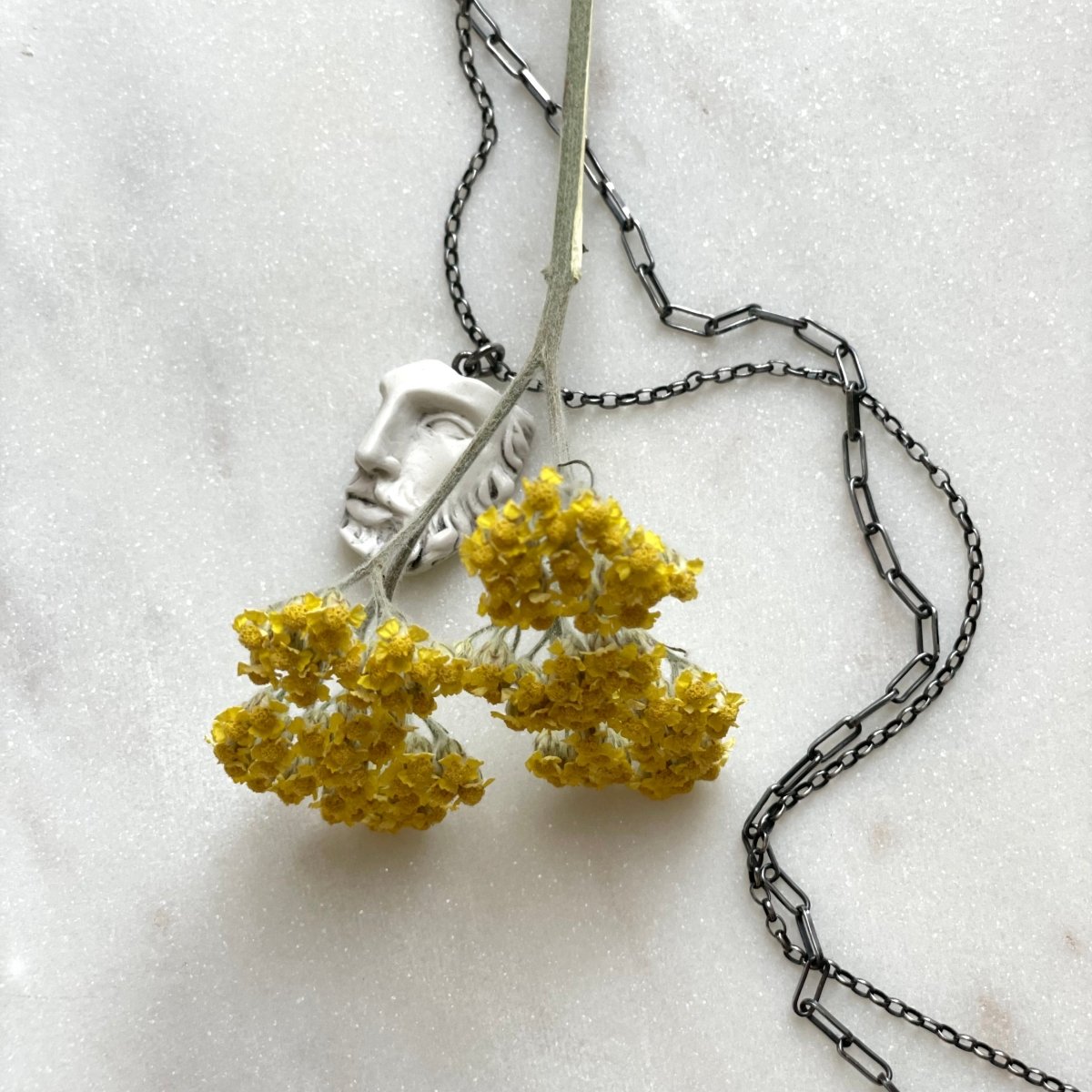 Heracles pendant and yellow flower on light-grey marble surface