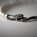 Ophidian Snake bracelet on a white surface, close up on a lock in shape of snake's head and tail, pearls are blurry