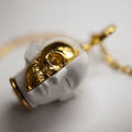 Oracle Skull pendant on its side, on white surface, both golden skull part and marble face part are visible