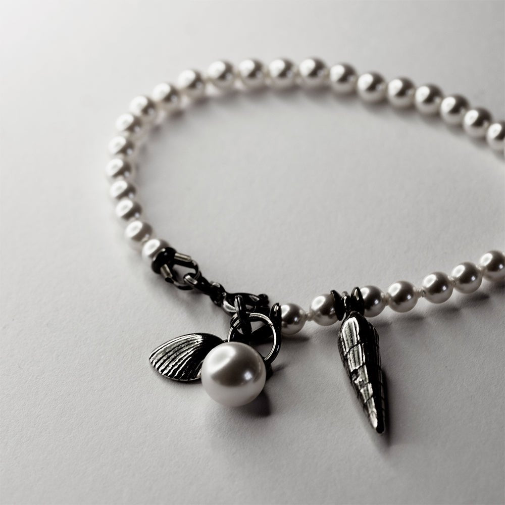 Pearl & Shell Bracelet - placed on a white surface - close up of shell charms and lobster clasp
