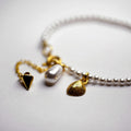 Pearl Bracelet - gold placed on a white surface, close up of shell charm and tear-drop pearl charm