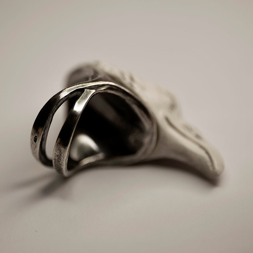 Raven ring - white variant - on its side on a white surface, focus on the sterling silver ring part