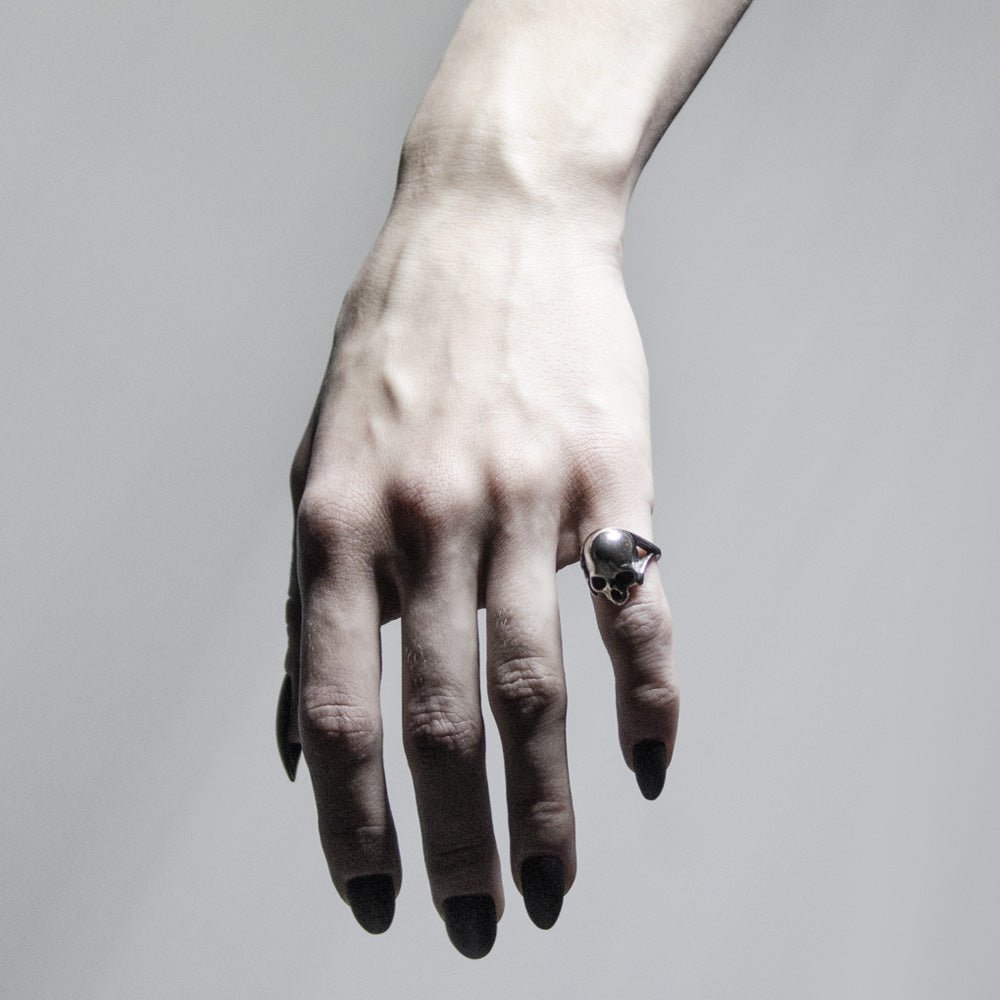 Silver skull ring on a woman's hand with long black nails, contrast light and monochrome palette align together creating striking mysterious image