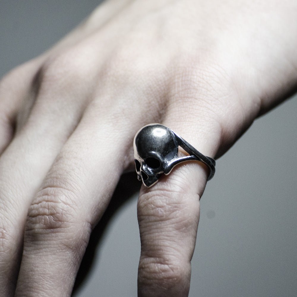 Silver skull ring on the man's hand, pinky finger, to demonstrate overall dimensions and fit