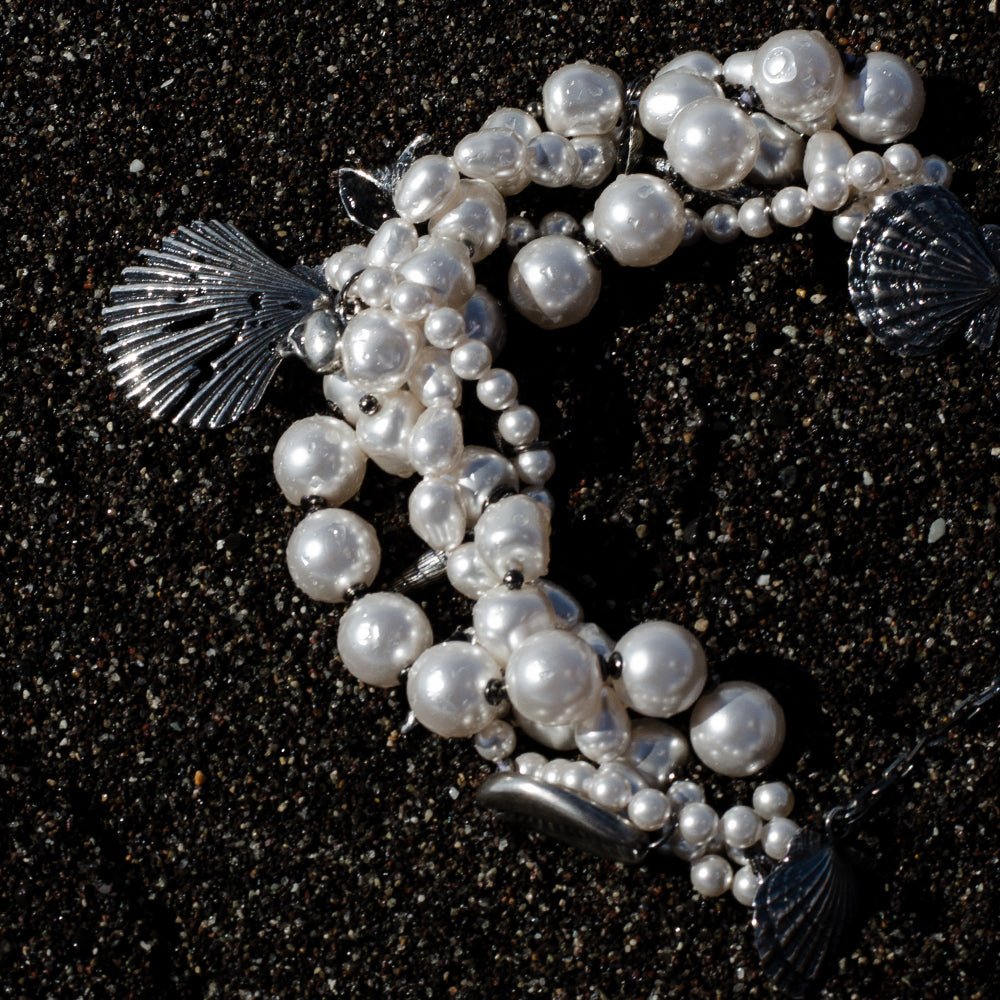 Siren Pearl Necklace submerged in a black sand on a sea shore, looks like a siren's necklace lost in storm