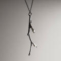 Silver Twig pendant against white surface with pearls visible