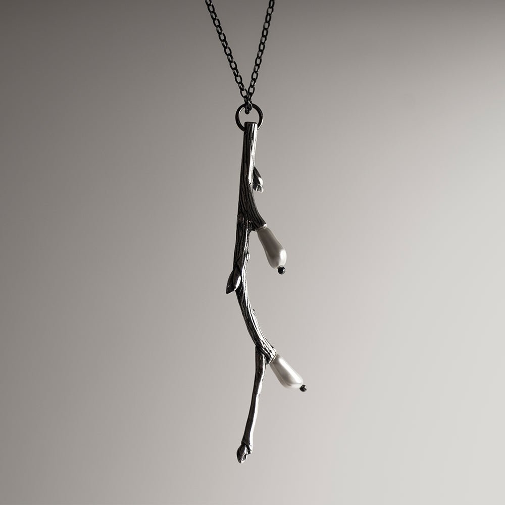 Silver Twig pendant against white surface with pearls visible
