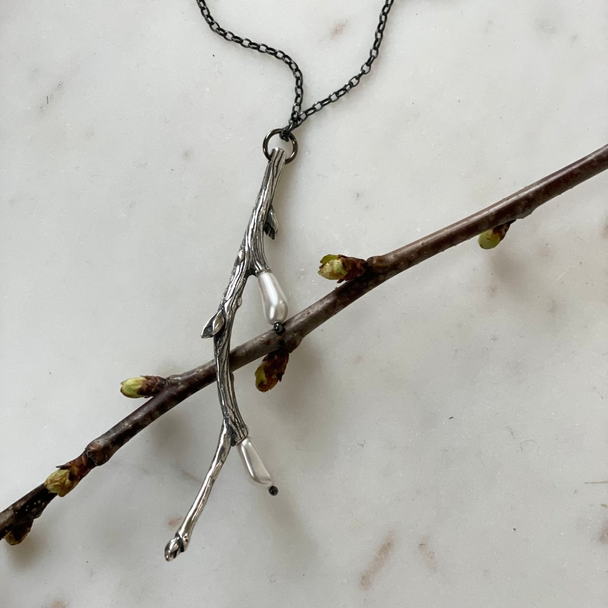 Silver Twig pendant on a marble surface together with real blooming twig