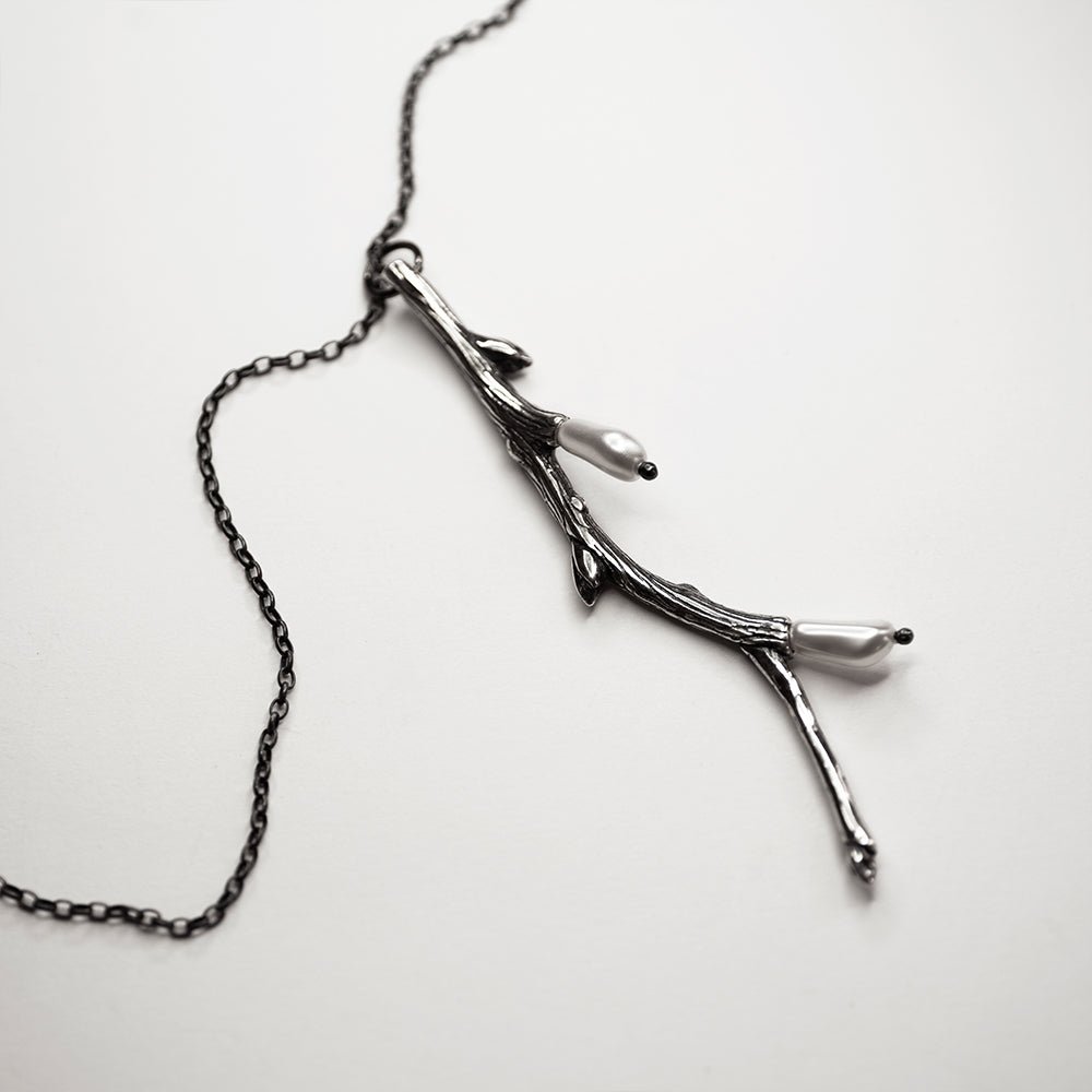 Silver Twig pendant placed on a white surface with fixture and chain clearly visible 