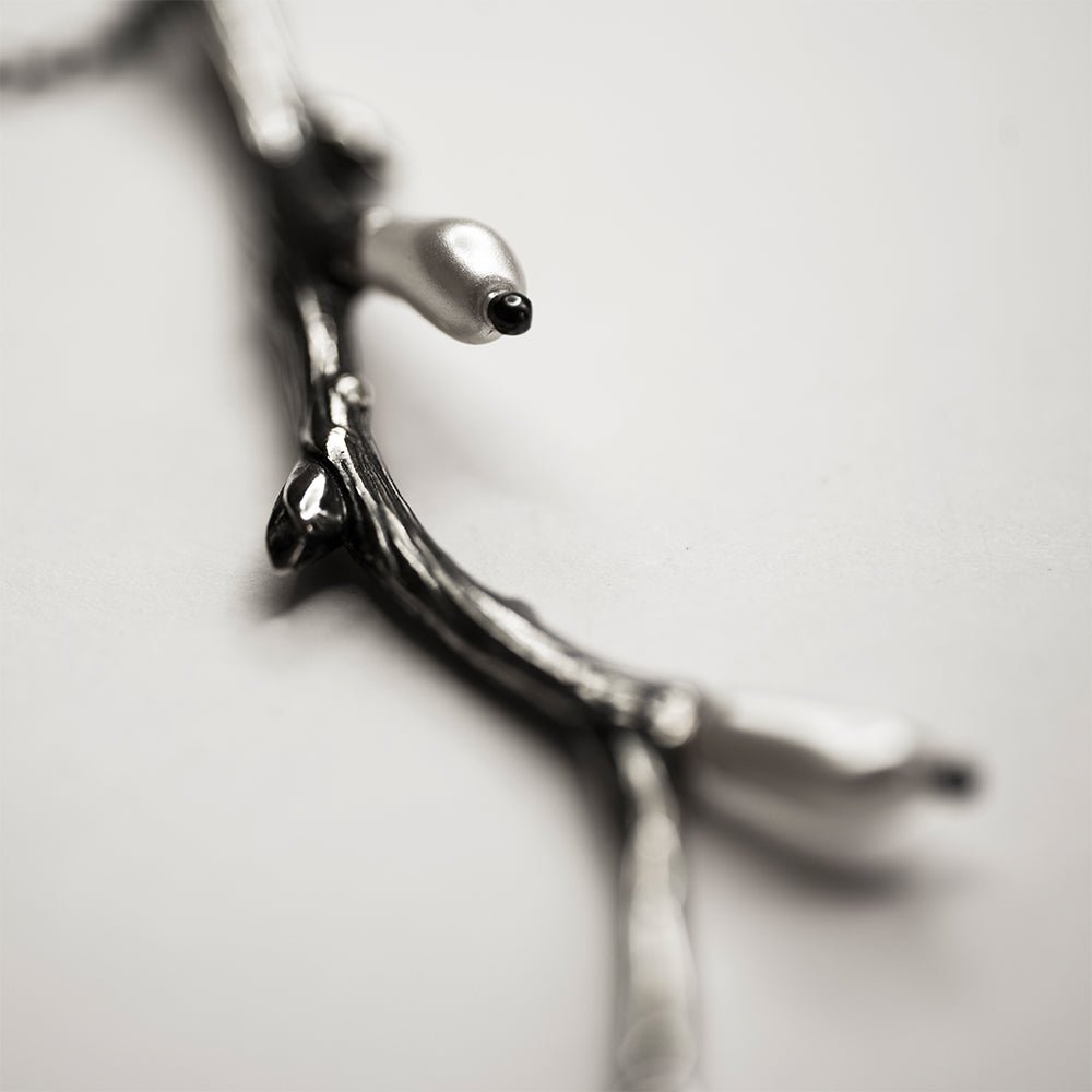 Silver Twig pendant close up on a pearls with rest of the pendant blurry 